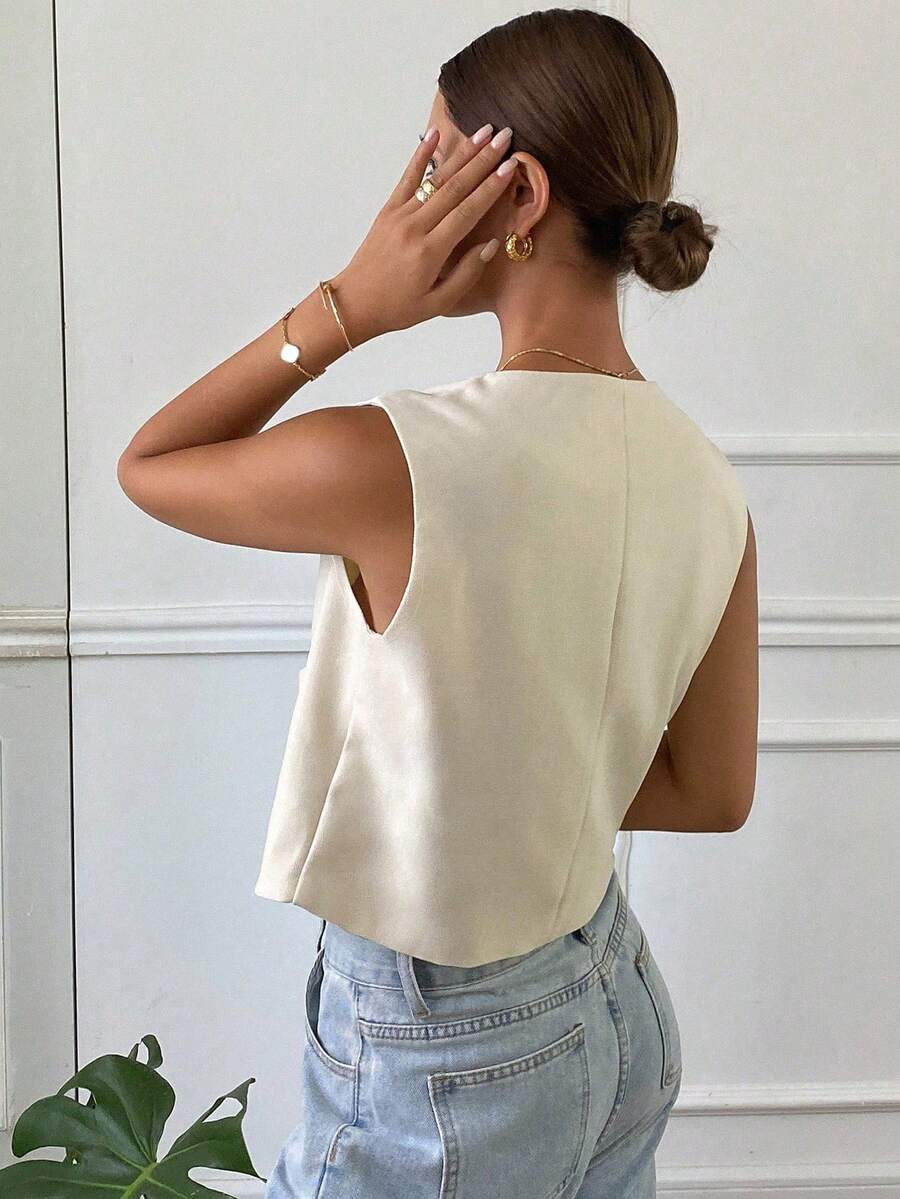 Mujer vistiendo un chaleco corto color crema con botones frontales y jeans de talle alto.