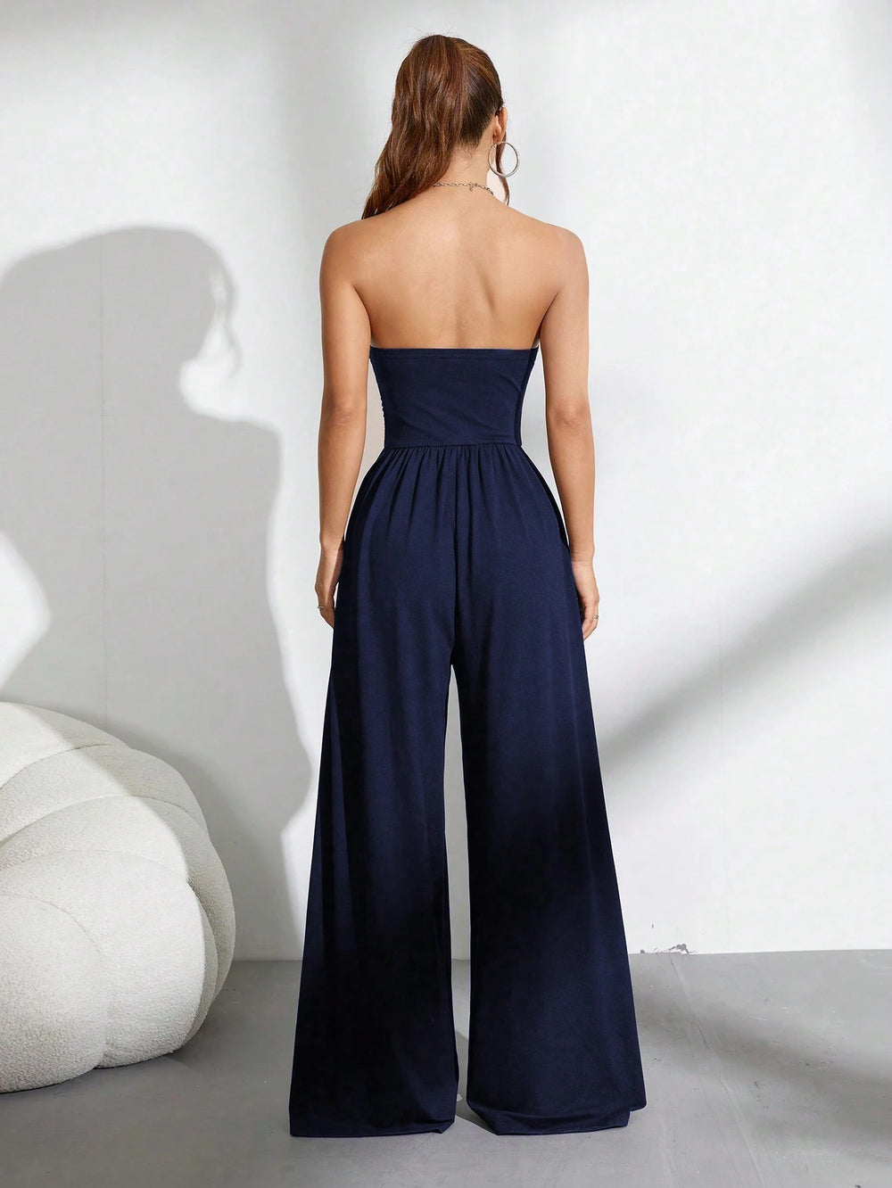 Mujer usando un mono largo azul marino sin tirantes y de talle alto, combinándolo con zapatillas blancas para un look casual.
