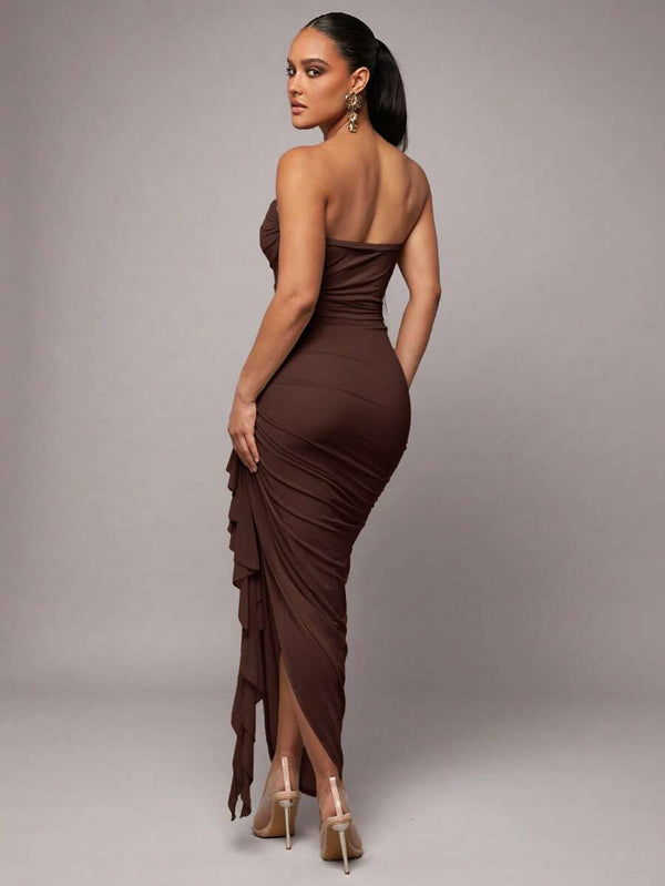 Modelo luciendo un vestido de fiesta ajustado color café con escote palabra de honor y falda asimétrica.
