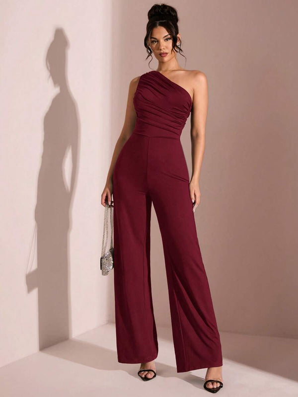 Vista completa de una mujer con un jumpsuit formal de un hombro y pierna ancha color vino.