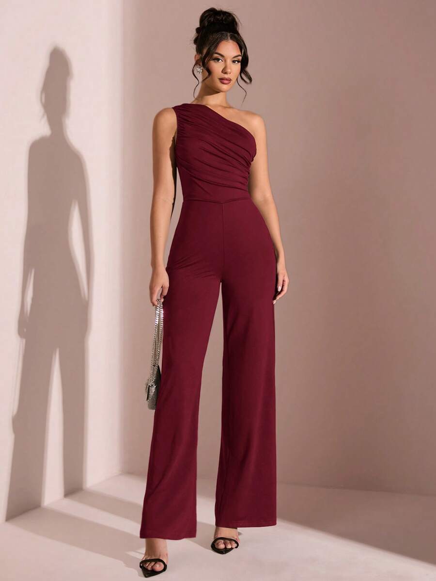 Mujer modelando un jumpsuit elegante color vino de un solo hombro con detalle drapeado.