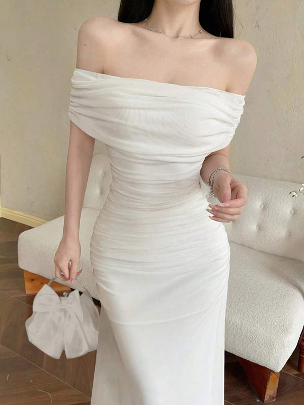 Modelo luciendo un vestido maxi blanco elegante con hombros descubiertos y fruncido, posando de pie.