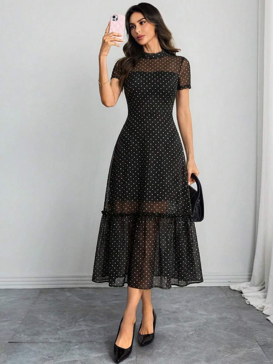Mujer posando de cuerpo completo con un vestido midi negro de lunares y malla transparente.