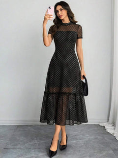 Mujer posando de cuerpo completo con un vestido midi negro de lunares y malla transparente.