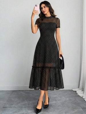 Mujer posando de cuerpo completo con un vestido midi negro de lunares y malla transparente.