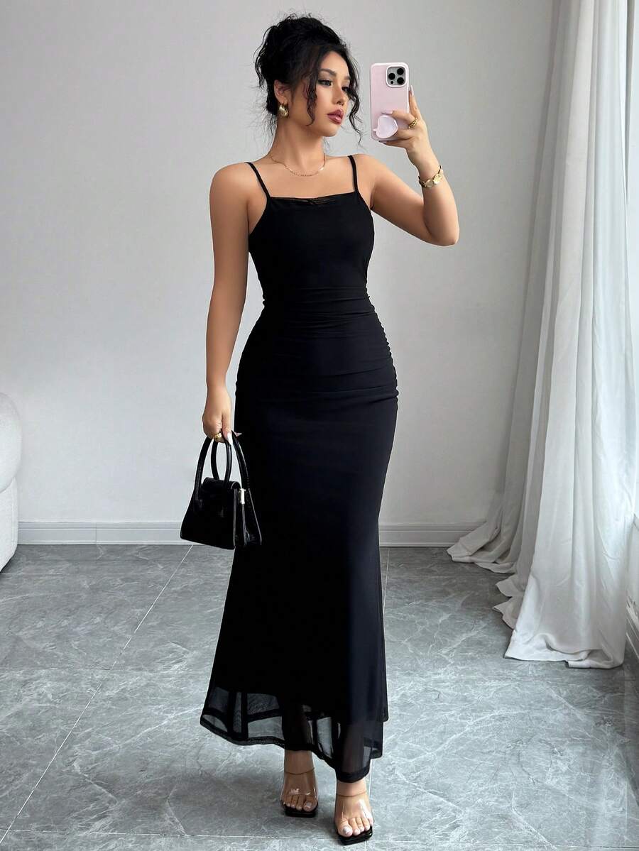 Mujer con vestido largo negro ajustado estilo sirena posando frente a un espejo.