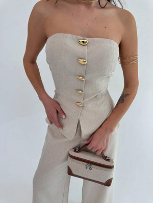 Primer plano del top tipo bustier strapless del conjunto beige con botones dorados decorativos.