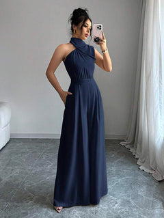 Mujer posando de cuerpo completo con un jumpsuit elegante azul marino de cuello halter y pierna ancha.