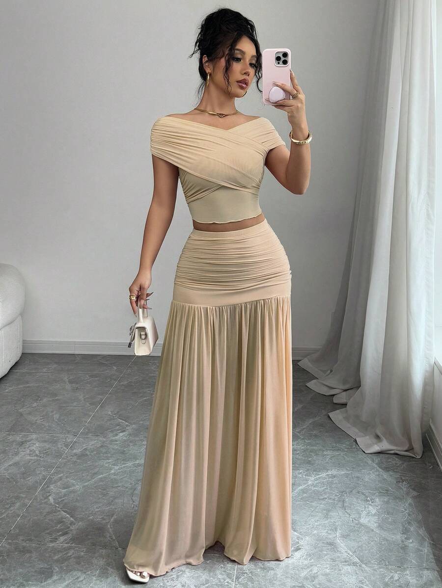 Mujer modelando un conjunto beige de dos piezas con top de hombros descubiertos y falda larga drapeada.