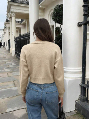 Vista del conjunto de cardigan corto beige combinado con jeans, mostrando una bolsa negra y manicura roja.