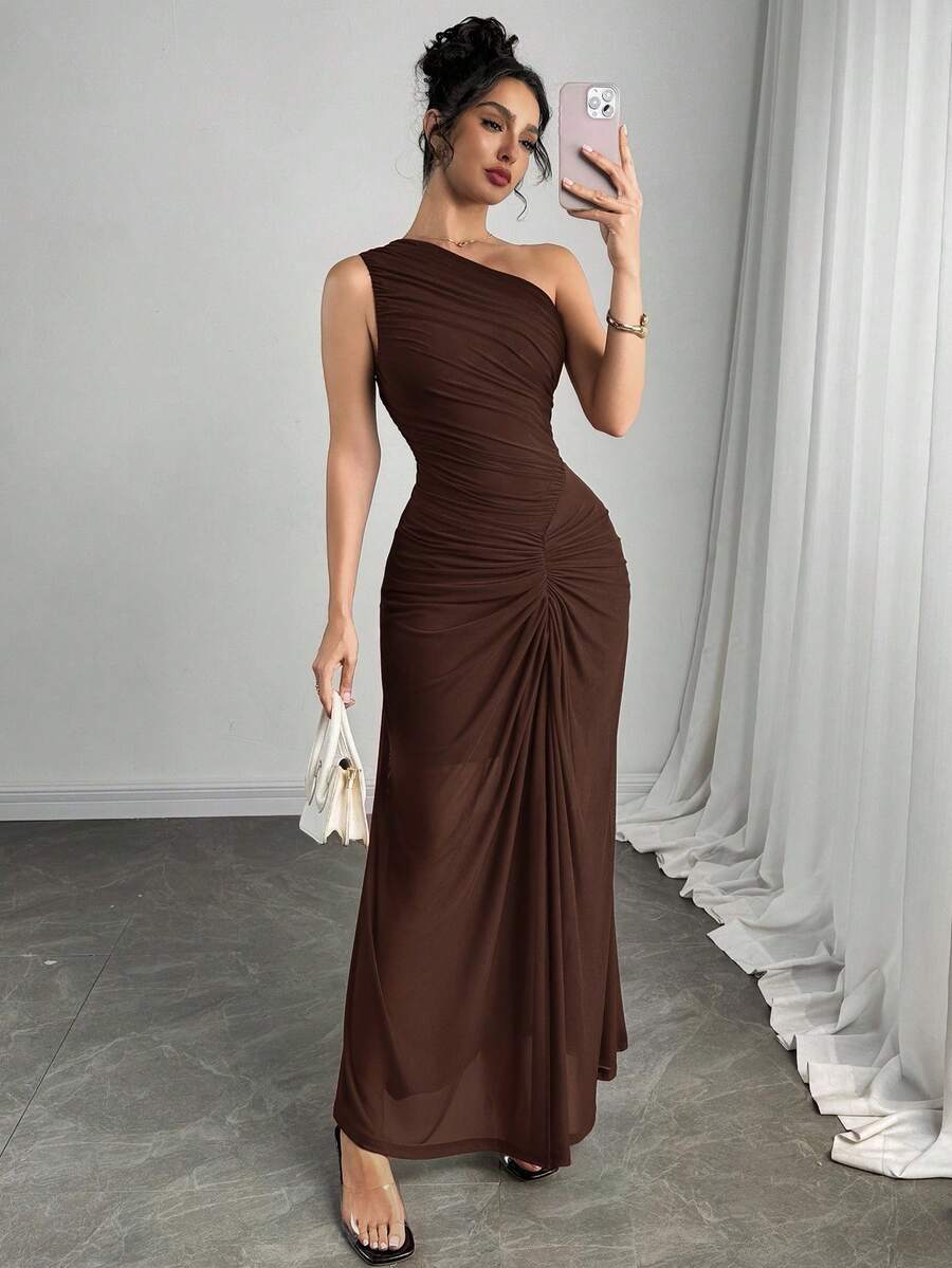Mujer posando de cuerpo completo con un vestido largo asimétrico color marrón y detalle fruncido.