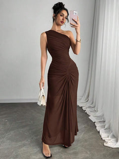 Mujer posando de cuerpo completo con un vestido largo asimétrico color marrón y detalle fruncido.