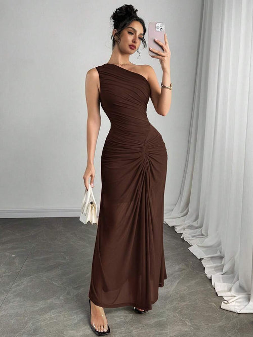 Mujer posando de cuerpo completo con un vestido largo asimétrico color marrón y detalle fruncido.