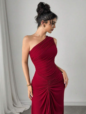 Detalle de la parte inferior del vestido maxi vino con fruncido y tela ligeramente transparente, junto a los pies y cartera.