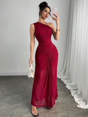 Modelo posando con vestido maxi vino de un hombro y detalle fruncido, con cartera blanca y sandalias transparentes.