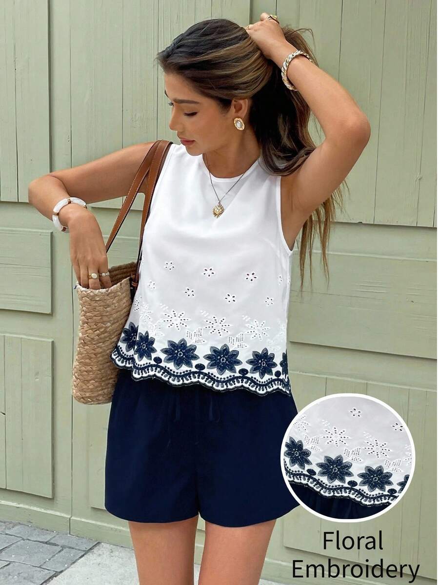 Mujer luciendo una blusa blanca sin mangas con bordado floral azul en el bajo, combinada con shorts azul marino.