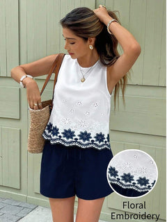 Mujer luciendo una blusa blanca sin mangas con bordado floral azul en el bajo, combinada con shorts azul marino.
