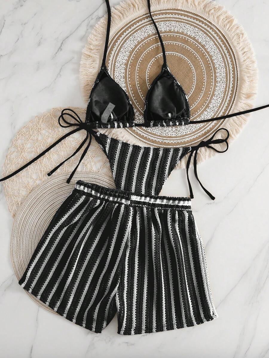 Conjunto de traje de baño de tres piezas a rayas blancas y negras sobre un fondo de mármol.
