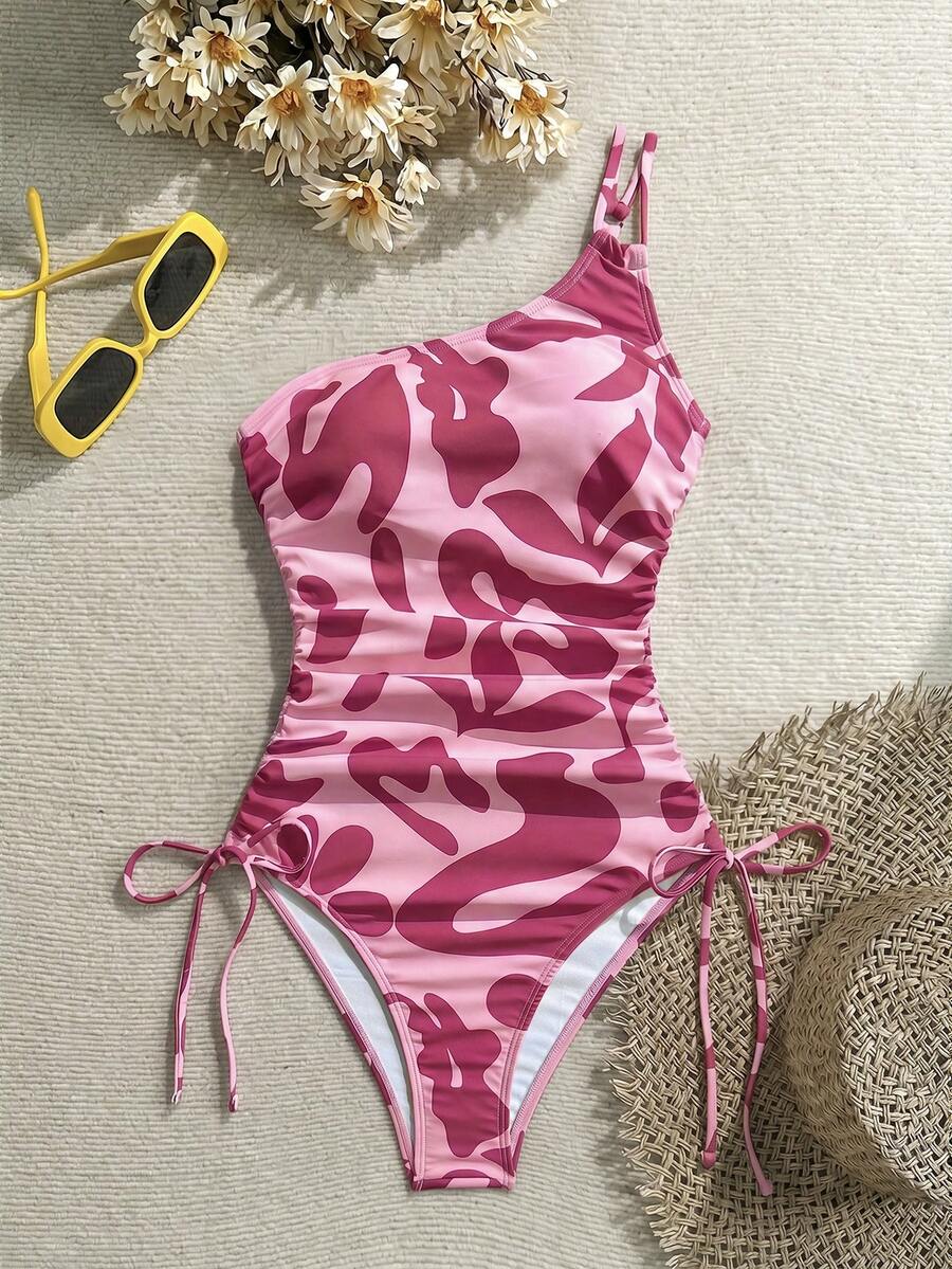 Traje de baño asimétrico de una pieza en tonos rosa con estampado abstracto y fruncidos laterales.