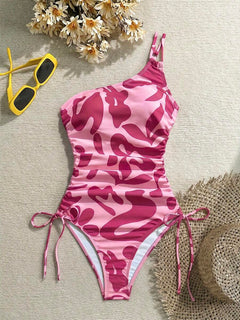 Traje de baño asimétrico de una pieza en tonos rosa con estampado abstracto y fruncidos laterales.