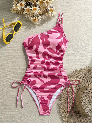 Traje de baño asimétrico de una pieza en tonos rosa con estampado abstracto y fruncidos laterales.