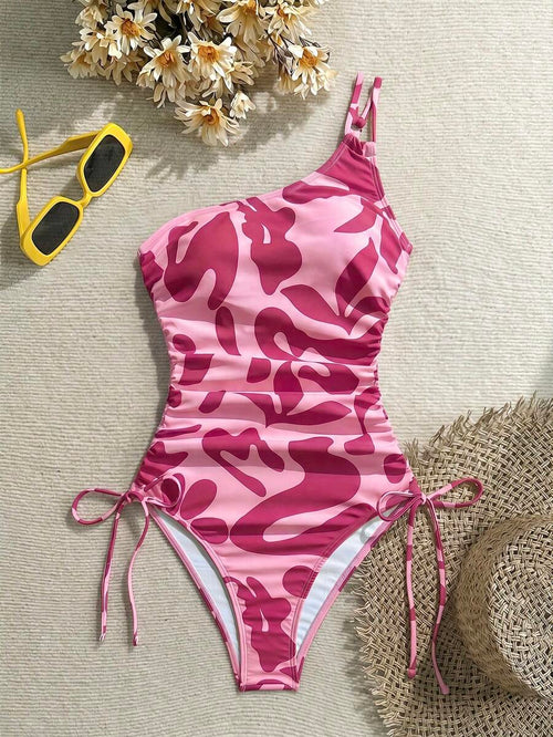 Traje de baño asimétrico de una pieza en tonos rosa con estampado abstracto y fruncidos laterales.