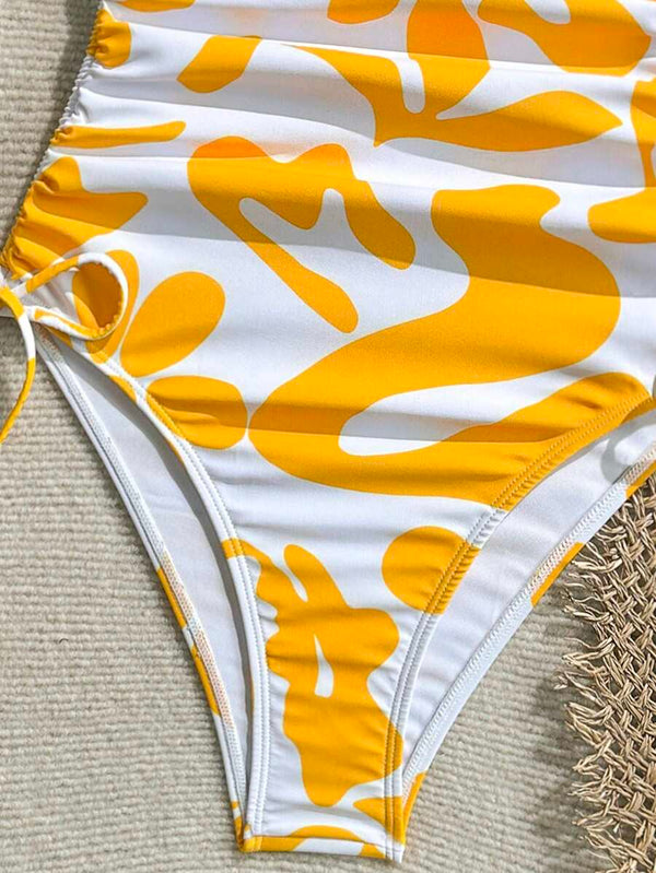 Vista del traje de baño de diseño asimétrico sobre un fondo veraniego con gafas de sol amarillas y sombrero de paja.