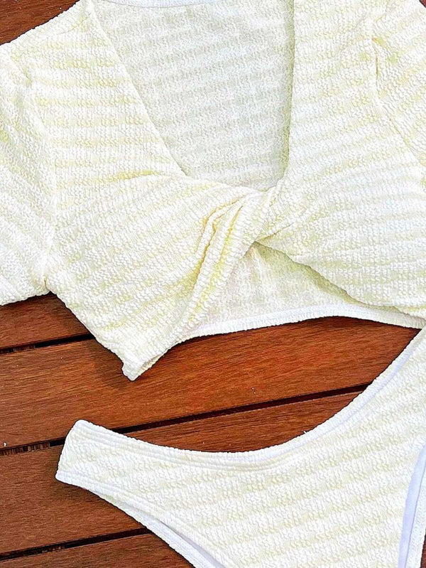 Mujer sentada luciendo un conjunto de bikini de dos piezas, top con mangas cortas y bottom de corte alto.
