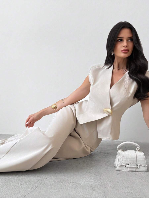 Mujer con conjunto elegante de chaleco y pantalón beige sentada en el suelo.