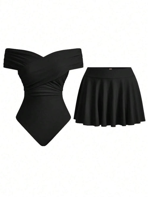 Conjunto de traje de baño negro de dos piezas con bañador de hombros descubiertos y falda corta acampanada, sobre fondo blanco.
