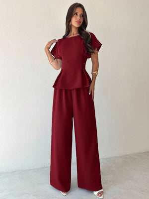 Mujer modelando un conjunto elegante de dos piezas color burdeos con blusa peplum y pantalón de pierna ancha.