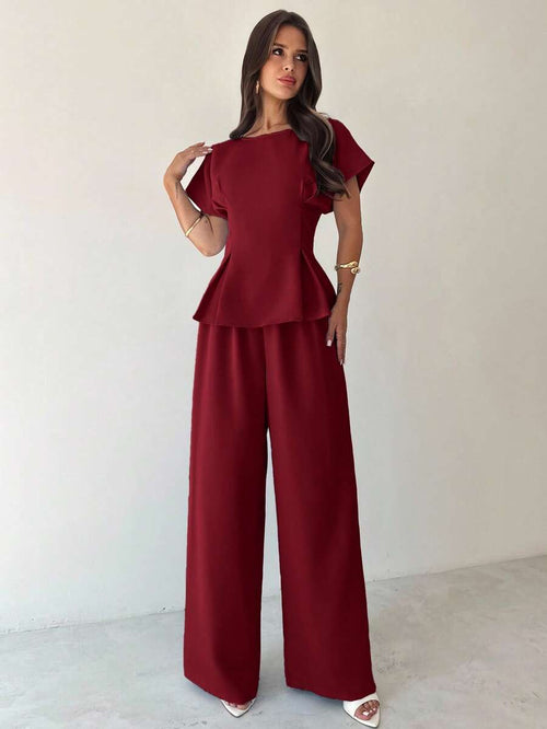 Mujer modelando un conjunto elegante de dos piezas color burdeos con blusa peplum y pantalón de pierna ancha.