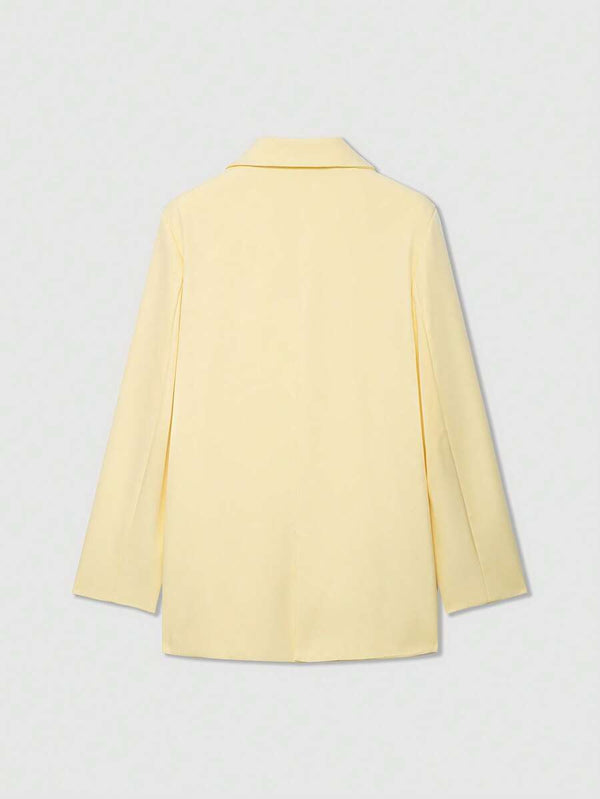 Detalle del cuello y la solapa de un blazer amarillo claro sobre fondo blanco.