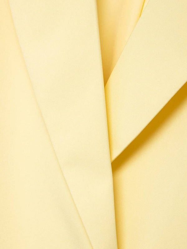 Primer plano de los bolsillos con solapa y los botones oscuros de un blazer amarillo.