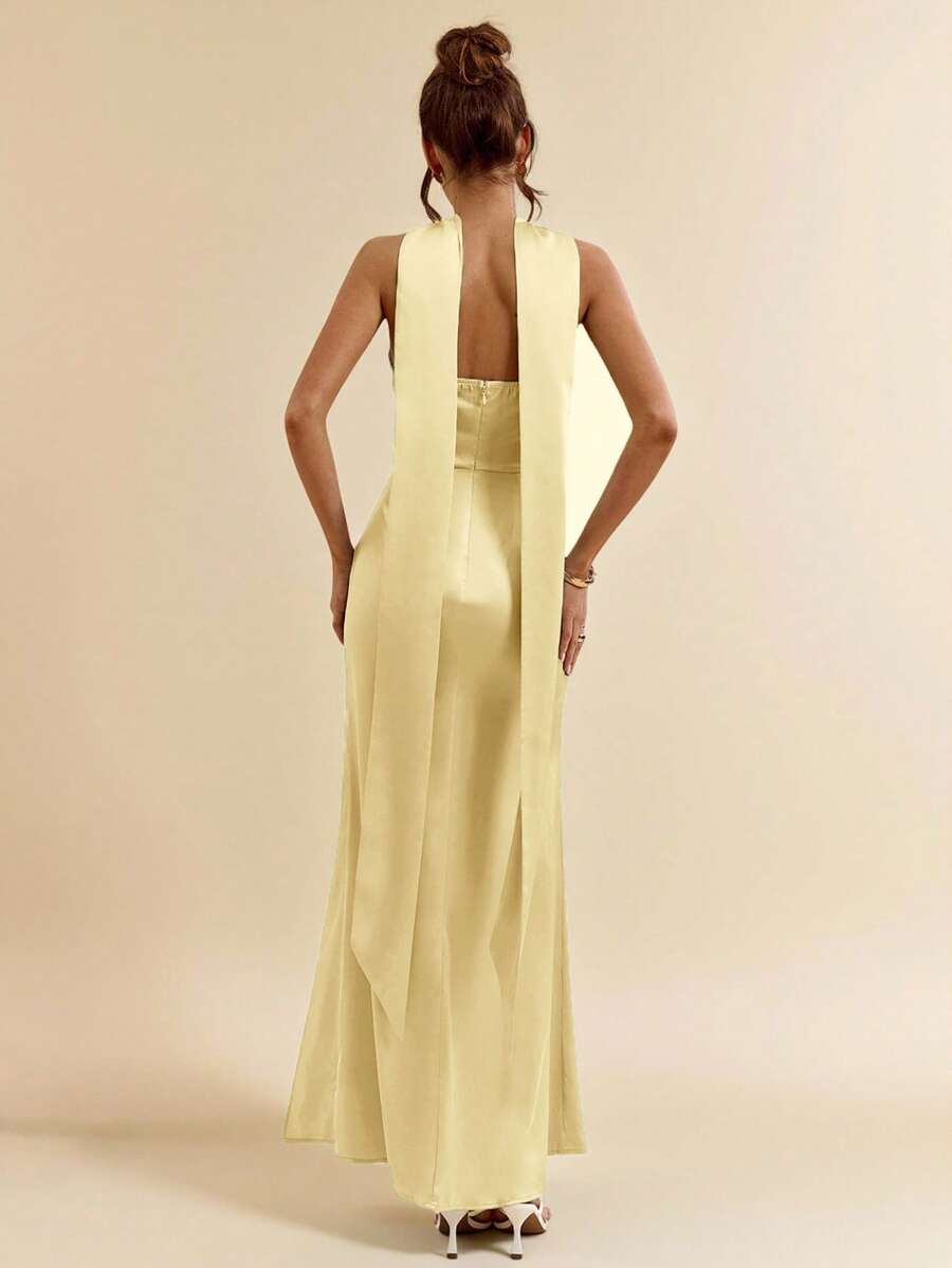 Mujer posando con un vestido largo satinado amarillo pastel de cuello halter y abertura lateral.