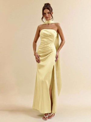 Parte inferior de un vestido largo amarillo con abertura en la pierna, combinado con sandalias blancas.