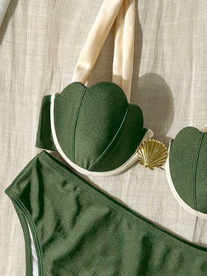Top de bikini verde oliva con copas en forma de concha y detalle dorado, sobre una superficie de tela clara.