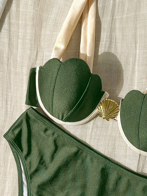 Top de bikini verde oliva con copas en forma de concha y detalle dorado, sobre una superficie de tela clara.