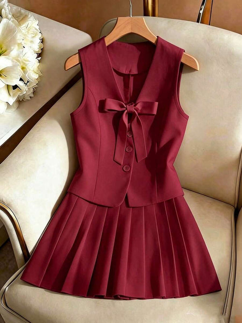 Conjunto de dos piezas color vino con chaleco y falda plisada colgado en una percha.