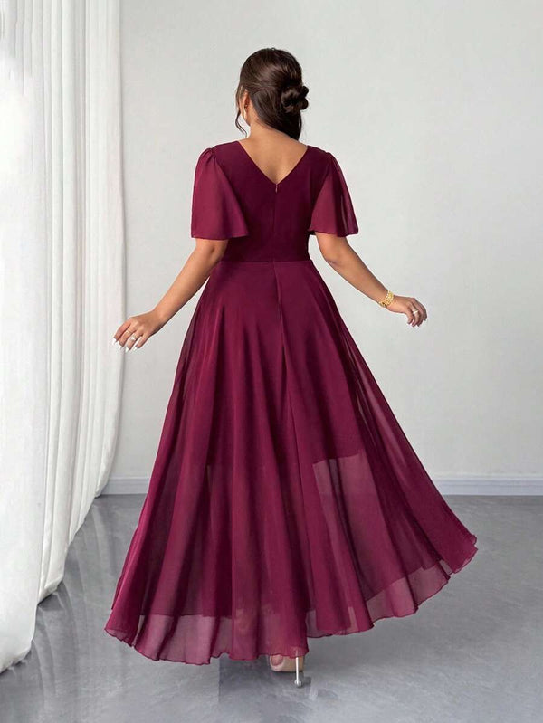 Primer plano del torso de una mujer con un vestido burdeos, destacando el escote cruzado y las mangas de gasa transparente.