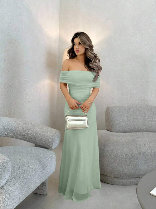 Mujer con vestido largo elegante color verde menta posando de pie en una sala moderna.