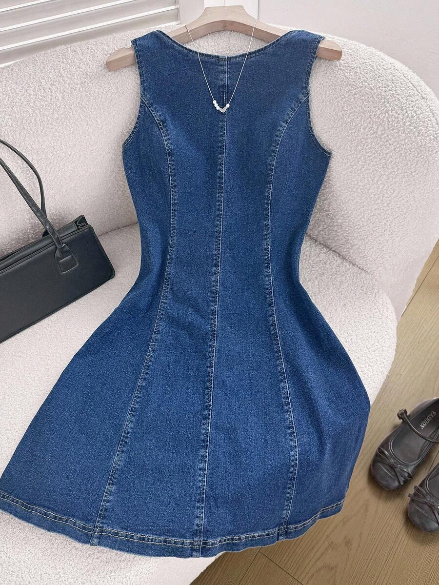 Vista frontal de un vestido de mezclilla azul oscuro sin mangas sobre una silla.