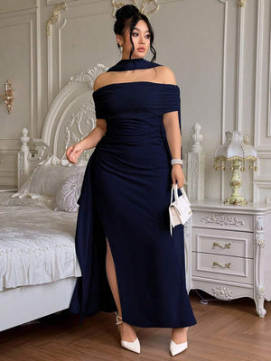 Mujer con vestido de noche azul marino de hombros descubiertos y abertura en la pierna, posando en un dormitorio elegante.