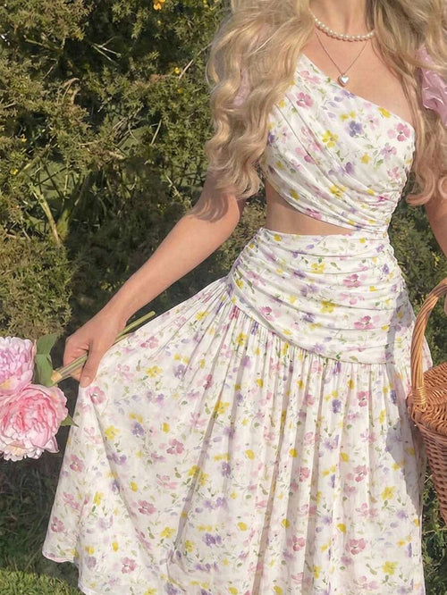 Mujer en un jardín luciendo un vestido blanco con estampado floral, escote asimétrico y falda midi.