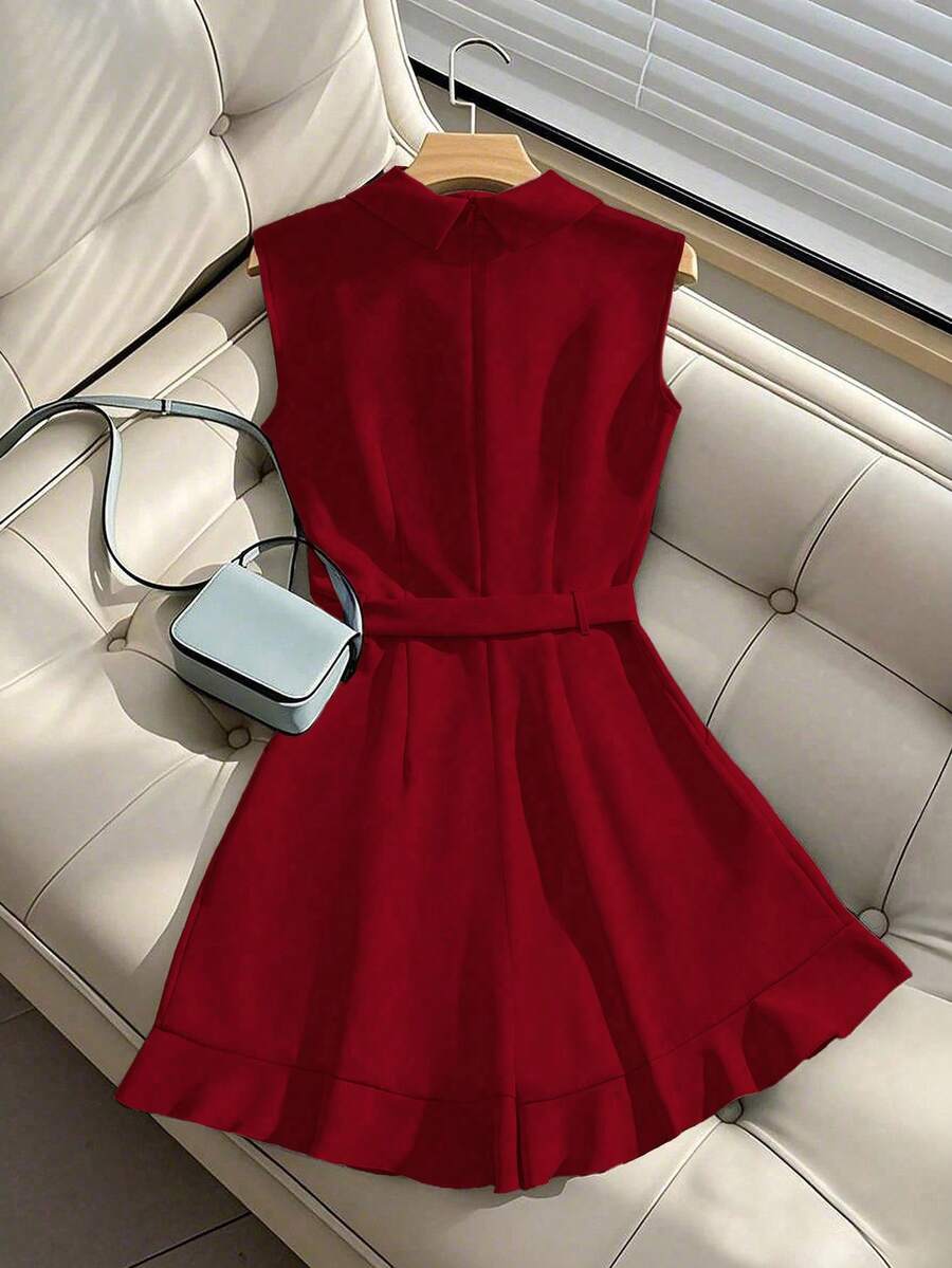 Romper elegante color rojo vino sin mangas con cinturón y escote de solapa, exhibido en un sofá blanco.