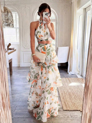 Mujer modelando un conjunto de dos piezas con estampado floral de naranjas y hojas verdes, compuesto por un top halter y una falda larga con volantes.