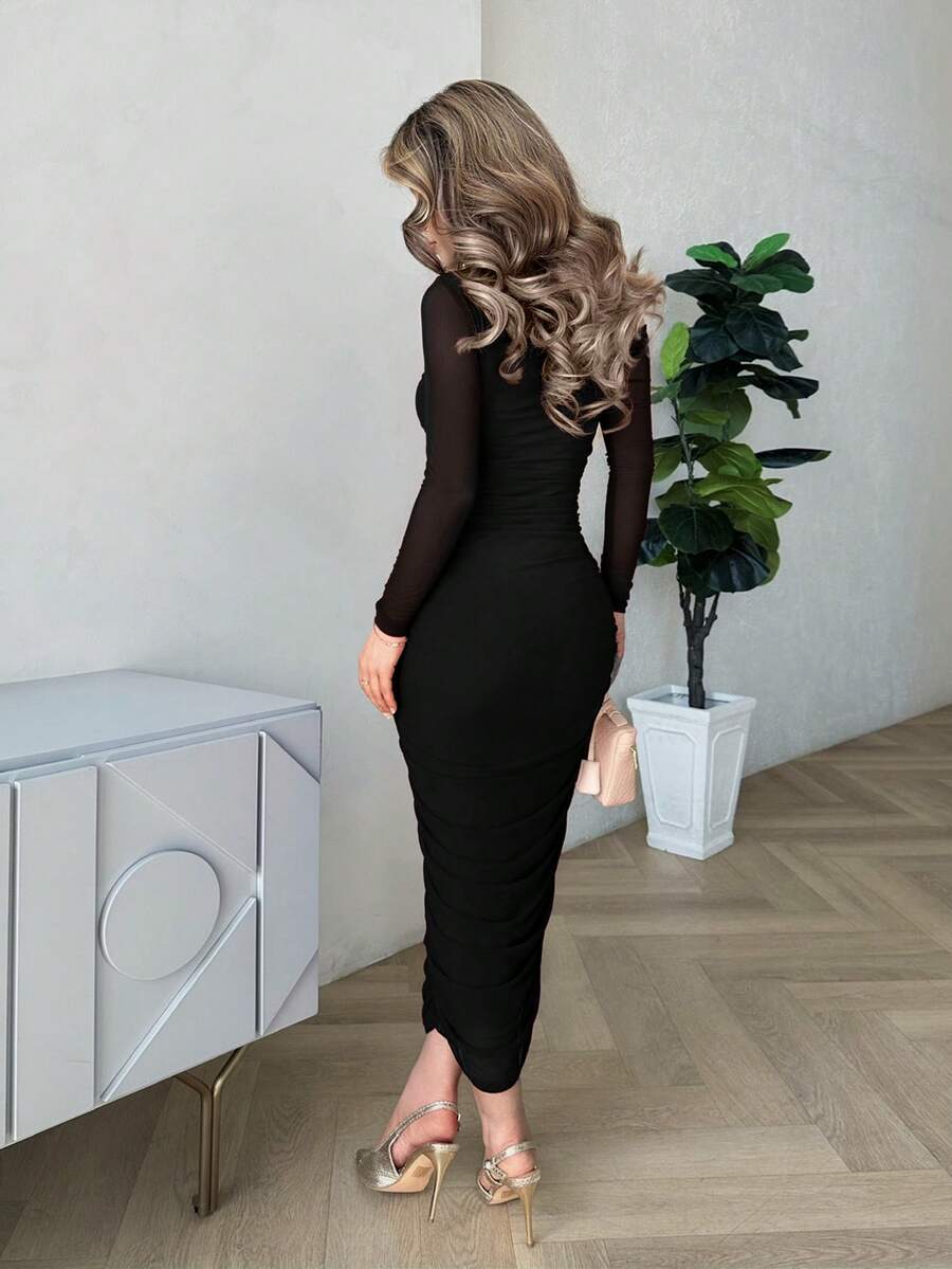 Mujer modelando un vestido midi negro ajustado con escote asimétrico y manga larga transparente.