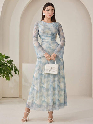 Mujer posando con un vestido largo estampado en tonos azules y blancos, de manga larga acampanada y cuello redondo.