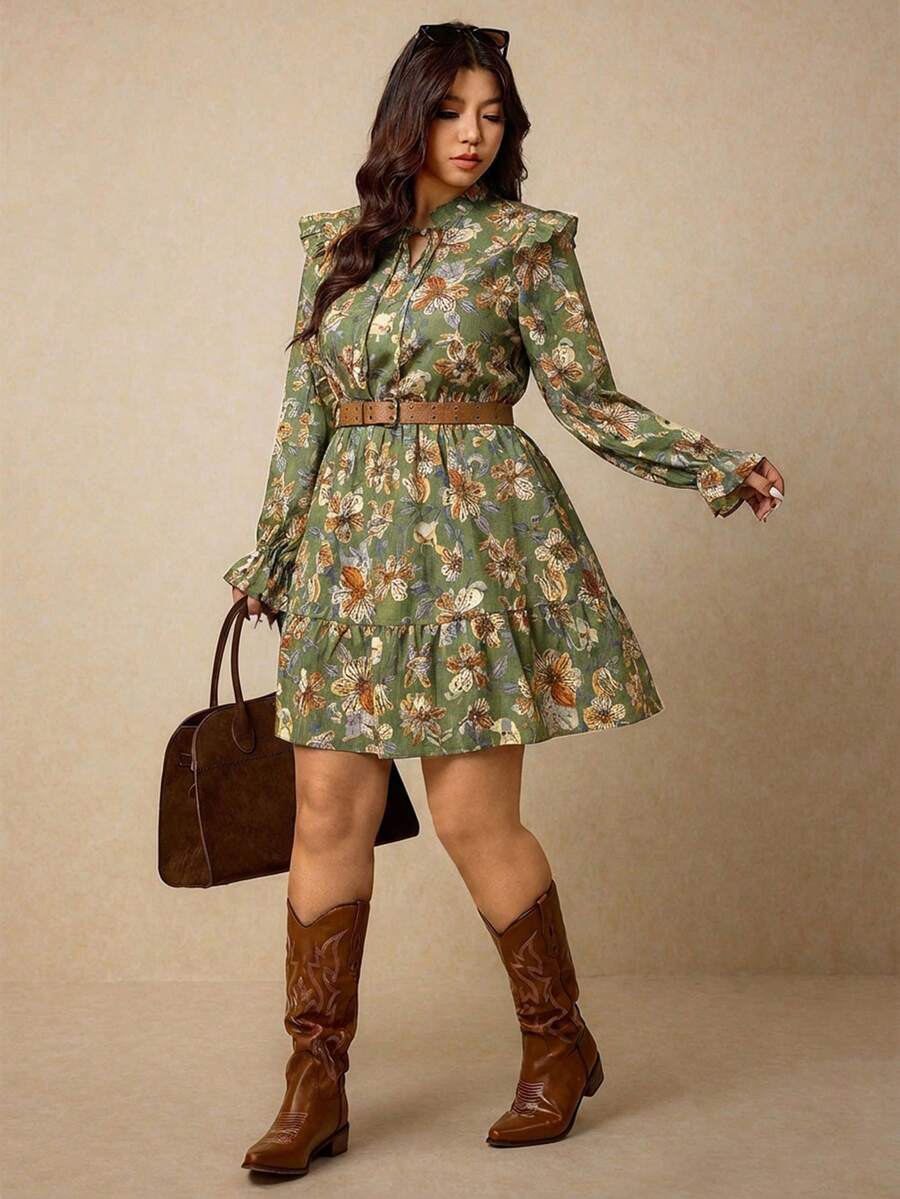 Modelo luciendo un vestido verde de estampado floral con volantes en los hombros, mangas largas y cinturón marrón.