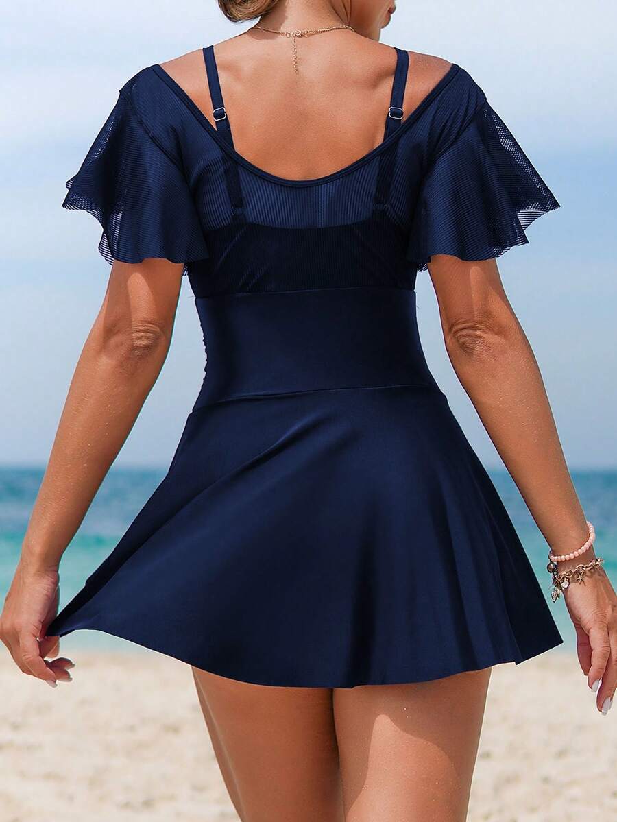 Mujer usando un traje de baño entero azul marino con falda y mangas de vuelo sentada en una silla de playa.